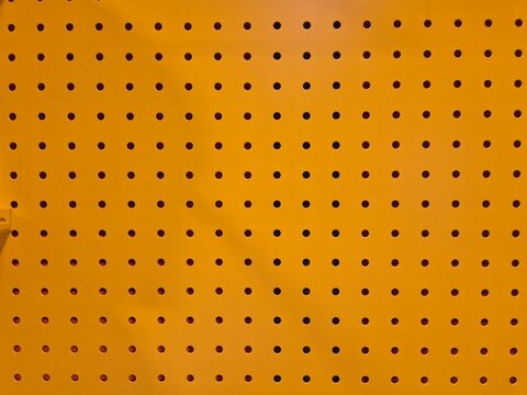 Bright orange pegboard with evenly spaced holes. Uniform pattern creates clean, industrial aesthetic. Ideal for storage, workshop, or creative project backgrounds
