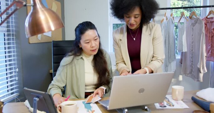 Diverse women team swapping swatches, marking samples with pink pen and checking laptop for design