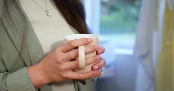 Starting with hands wrapping white ceramic mug, woman is cradling it near window while stabilizing