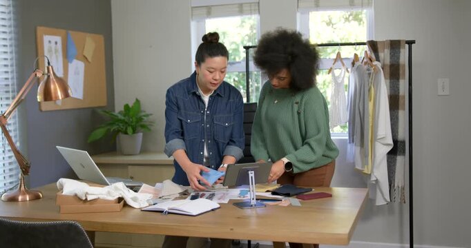 Women designers showing blue swatch, arranging samples, tapping tablet, choosing colors at table