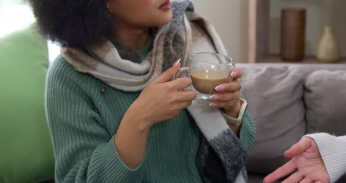 African American woman holding glass mug, speaking then listening on couch, responding to gestures