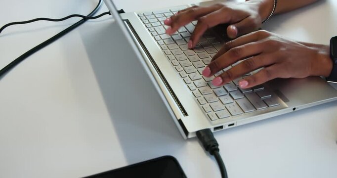 Female hands are typing after fingers press keys on silver laptop at white desk for work