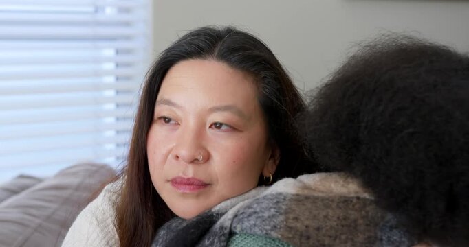 Diverse women on couch at home, other leaning in, woman white sweater closing eyes for comfort