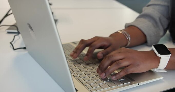 Woman's hands are hovering then typing on silver laptop at office desk, finishing work document