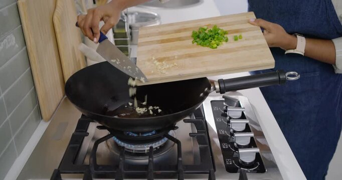 Cook is placing wok on burning gas burner and scraping garlic into oil to flavor food
