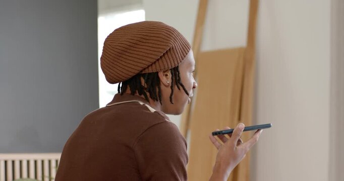 Adult man sitting at home wearing brown beanie, holding phone at mouth, responding to voice prompt