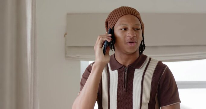 Adult male answering call by window, lowering phone and scrolling, checking texts in brown beanie