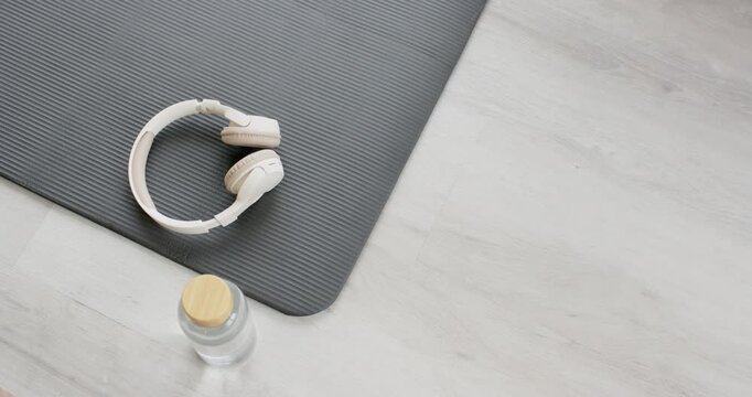 Camera is shifting, revealing gray mat with headphones and water bottle, staying ready for workout