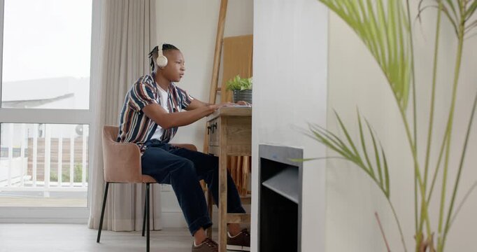 African American man pausing after typing on laptop at desk stretching for neck relief with headset