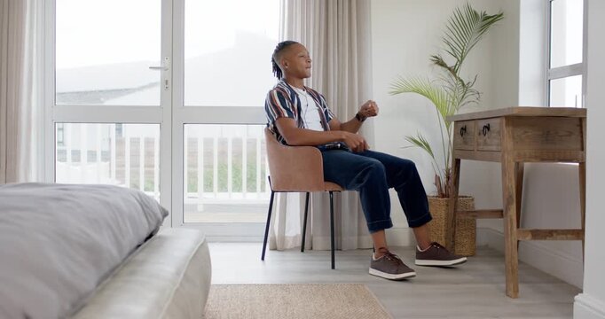 African American man sitting in chair in bedroom, hands resting, miming driving motions practicing