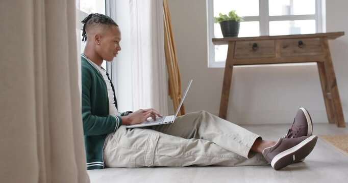 African American man settling near window, typing and adjusting hands on laptop, studying at home