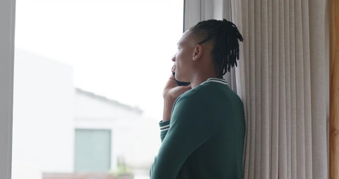 African American man leaning right at window taking call, holding phone, listening, copy space