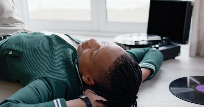African American man lying on floor near window bathing in sunlight resting by turntable records