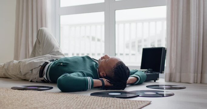 African American man lying on floor at home, listening to vinyl, turntable playing to relax