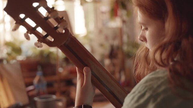 Cinematic close-up of a young redhead girl playing a classical guitar. The shot focuses on the wooden headstock in the foreground, with her focused profile softly blurred in the warm, sunlit 