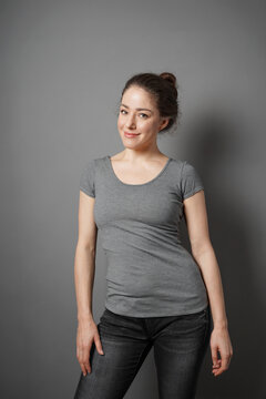 casual young adult woman with friendly smile wearing grey fitted t shirt with black denim jeans and brunette hair bun