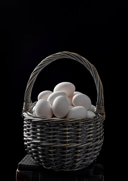 white eggs in wicker basket on black background