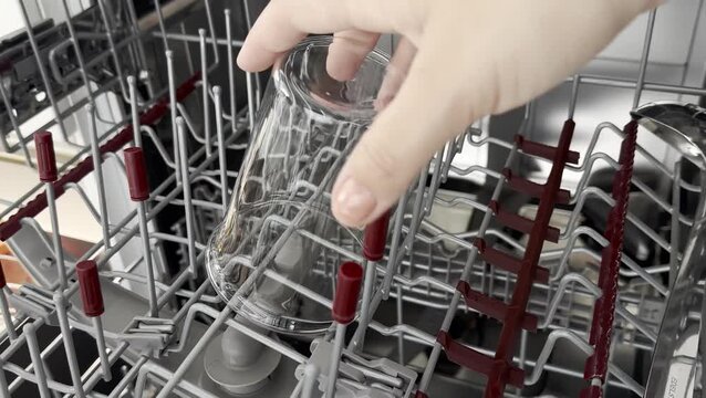 Close up of a female hand empty out the clean glass cups from a dishwasher rack