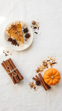A slice of pumpkin pie and spices arranged on a white cloth, symbolizing autumn harvest and festive baking, with free space for text