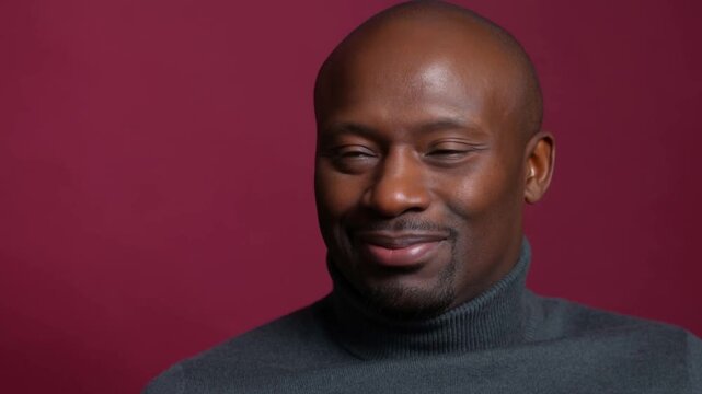 Man squinting with a skeptical expression in gray turtleneck against burgundy background