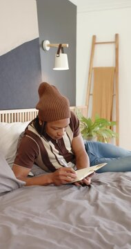 Vertical video: Man lying on bed holding notebook in lap, taking notes with pen and adjusting pages