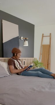 Vertical video: African American adult male opening blue book and reading for rest reclining in bed