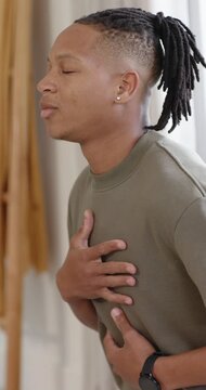 Vertical video: African man placing hands on chest and belly, breathing near window wearing watch