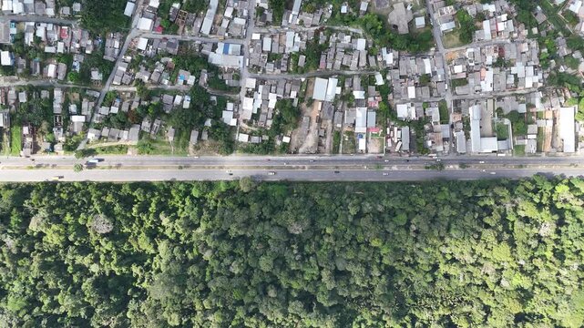 Top-down aerial view showing a stark contrast between a dense urban neighborhood and a lush green tropical forest in Brazil.