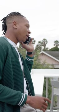 Vertical video: African American man taking phone call, pointing, gesturing on balcony, copy space