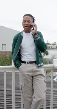 Vertical video: African adult male taking call, leaning on balcony railing, on phone, checking in