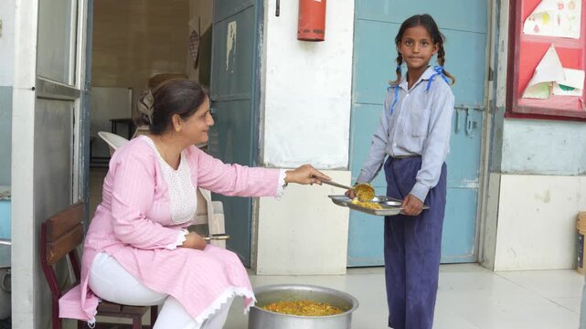 Indian teacher serving nutritious mid-day meal to a female student. food security and well-being for underprivileged children in school of india.