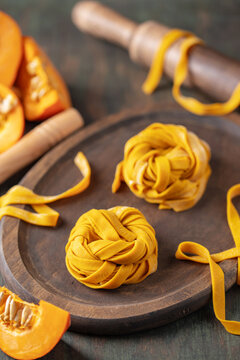 Homemade uncooked pumpkin tagliatelle or fettuccine noodles on a wooden board