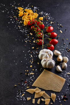 Ingredients for cooking pasta on a black background. Pasta, sherry tomatoes, garlic, cheese, pepper and salt.