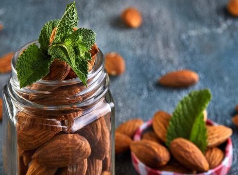 Almonds in a transparent jar with sheets of mint on the top on a background with a blue tint.