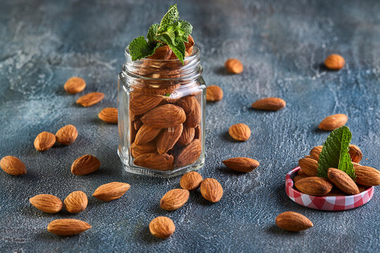 Almonds in a transparent jar with sheets of mint on the top on a background with a blue tint.
