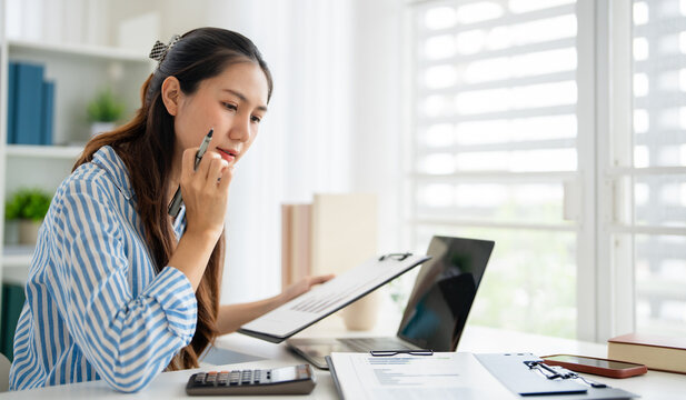 Young asian woman review paper documents, managing business affairs, summarizing taxes, planning future investments, accounting at home office.