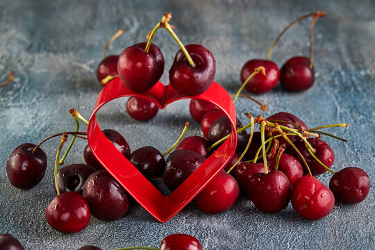 Fresh Cherry or sweet cherry with water drops with a red heart, lying on a background with a blue tint. Concept for valentines day