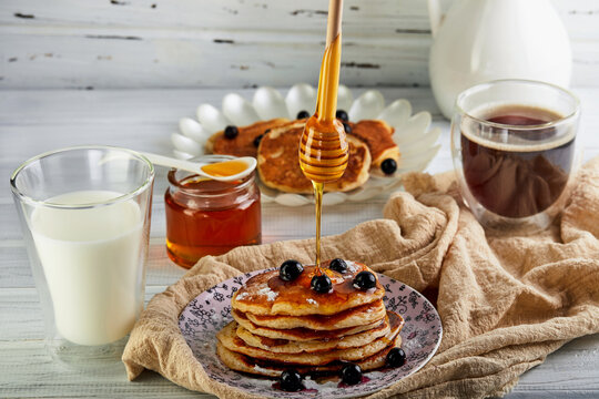 Tasty breakfast. A stack of pancakes with honey syrup a glass of milk, espresso coffee and honey on a wooden white background