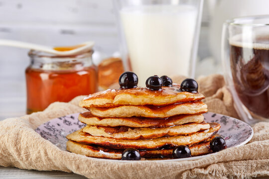 Tasty breakfast. A stack of pancakes with honey syrup a glass of milk, espresso coffee and honey on a wooden white background