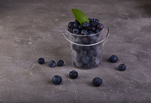 Fresh blueberries in a transparent bucket on a gray concrete background