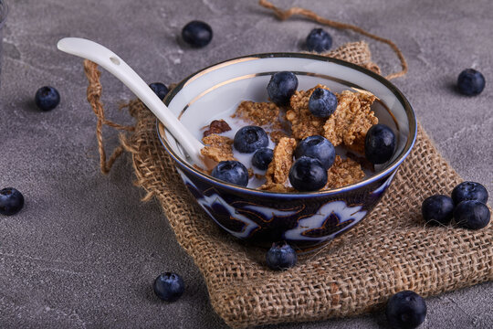 Fresh blueberries and a bowl with cornflakes and milk on a gray concrete background