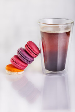 Fresh macarons of different colors and flavors and a glass of espresso coffee on a white background with reflection