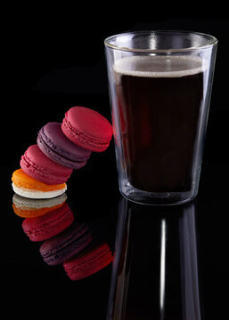 Fresh macarons of different colors and flavors and a glass of espresso coffee on a black background with reflection