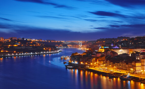Porto, Portugal. Evening sunset panoramic view at nighttime town and Ponte de Dom Luis bridge with tramways. Coastline of river Douro with reflections of illumination in water and picturesque clouds.