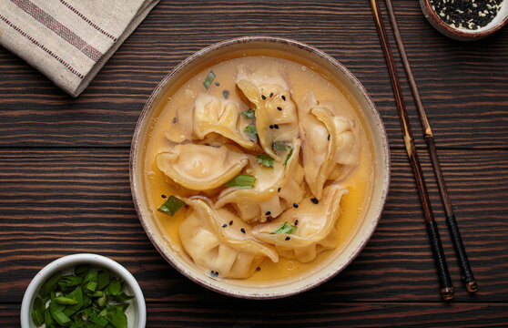 Gyoza dumplings broth soup chopsticks wooden background bowl asian wontons