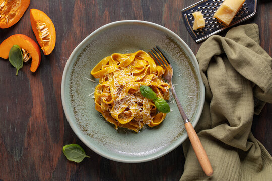 Homemade pumpkin tagliatelle pasta with parmesan cheese in a plate on the table. Italian cuisine. Top view