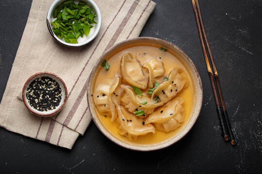 Gyoza dumplings broth soup chopsticks dark background bowl asian wontons