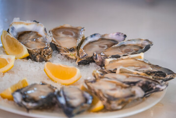 A platter of fresh opened oysters on the half shell arranged on crushed ice with yellow lemon wedges in a restaurant. © Aerial Film Studio