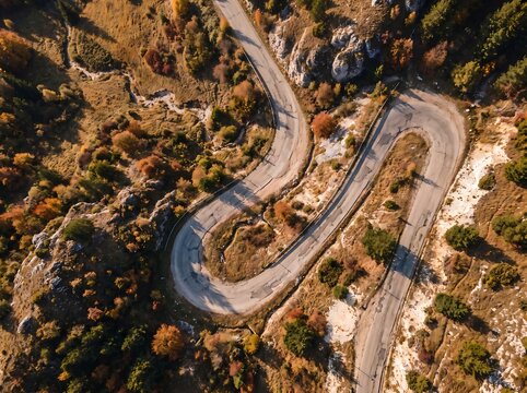 Aerial top down view of a winding road across rocky terrain and autumn foliage hills with landscape transportation environment