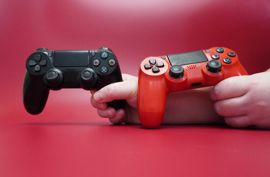 Two PS4 gamepads in his hands on a red background. Black and red DualShock 4, front view.
